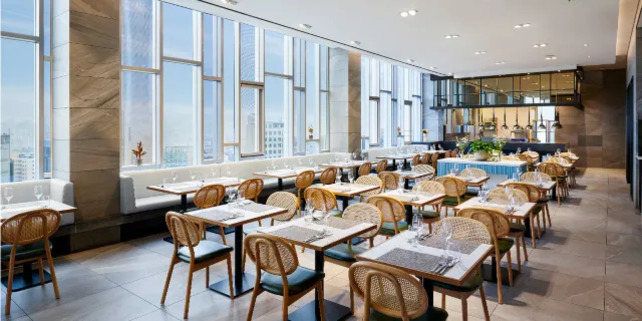 넓고 현대적인 인테리어의 레스토랑 내부, 큰 창문으로 자연광이 들어오고 여러 개의 테이블과 의자가 정돈되어 있다.