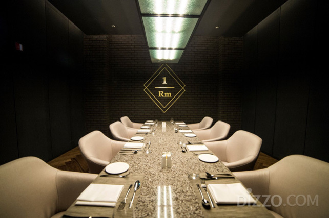 고급스러운 분위기의 프라이빗 다이닝룸에 긴 테이블과 8개의 의자가 놓여 있고, 테이블 위에는 식기와 냅킨이 정갈하게 세팅되어 있다. 벽에는 '1 Rm'이라는 표식이 보인다.